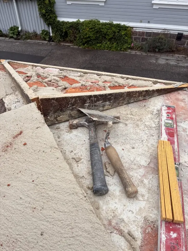 Hammare, murslev och tumstock på ett murkrön under renovering